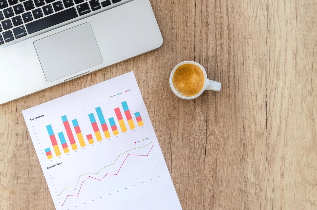 Laptop, coffee and a printed marketing report on a wooden desk