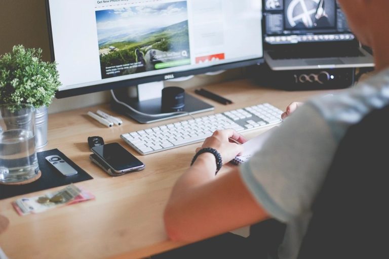 Designer working at a desk with a large monitor and laptop