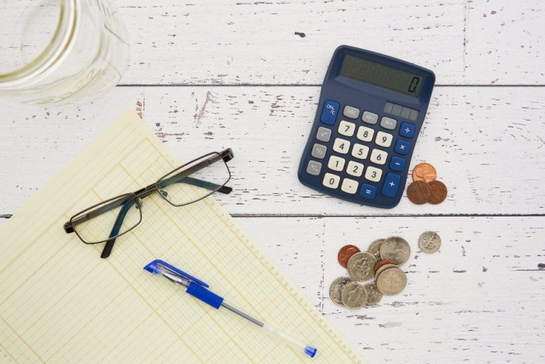Calculator, glasses, pen and coins on a notepad